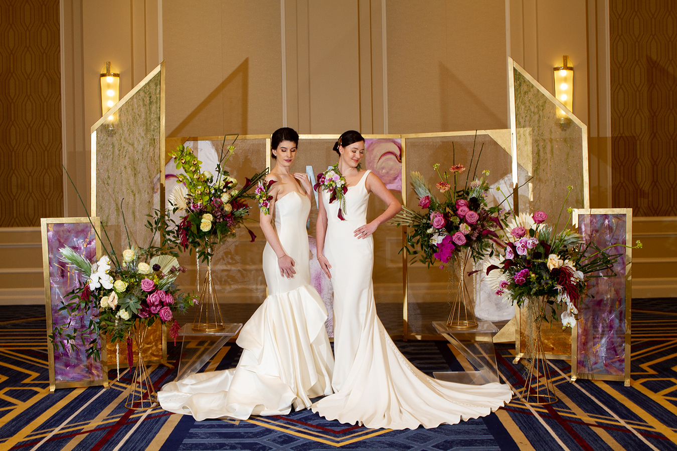 Julie and Kaylei pose in front of a series of hand-painted screen backdrops amid lush florals from Mitch’s Flowers. Both women wear elegant floral pieces, alternatives to traditional bouquets, designed by Mitch’s Flowers. A custom-made monogram from Design A Latte Monograms is suspended from the center backdrop panel. Julie’s classic strapless Mikado silk gown is from Pearl’s Place with a diamond bangle, pearl stud earrings, contour baguette band with pear-shape diamond solitaire ring and an Art Deco studded band from Brilliance in Diamonds. Kaylei is wearing a simple, modern fit-and-flare gown from MaeMe The Bridal Boutique with a diamond bangle bracelet, “Marigold” ring and radiant cut diamond studs from Brilliance in Diamonds.