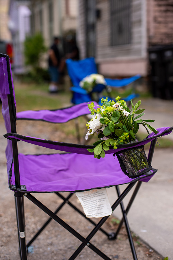 Parade chairs with flowers, placed six feet apart on the sidewalk, serve as seating for the wedding guests.