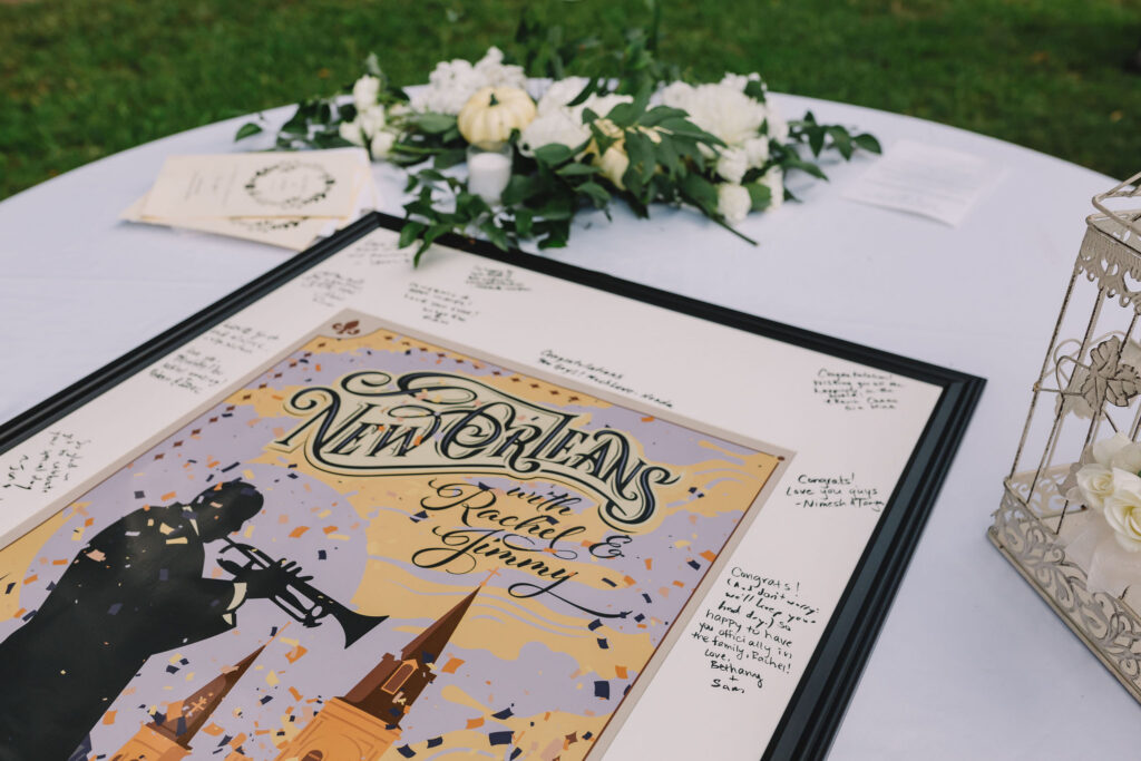 Framed New Orleans print on table with congratulatory cards, white flowers, greenery, and wedding programs outdoors.