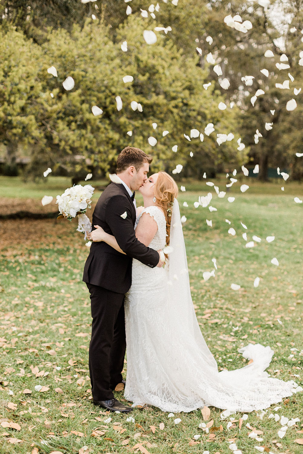 bride and groom kissing with flower petals in the air