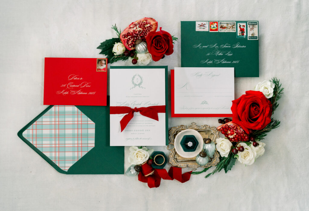 Holiday stationery with red, green, and white invitations, roses, flowers, pomegranate halves, stamps, and plaid lining.