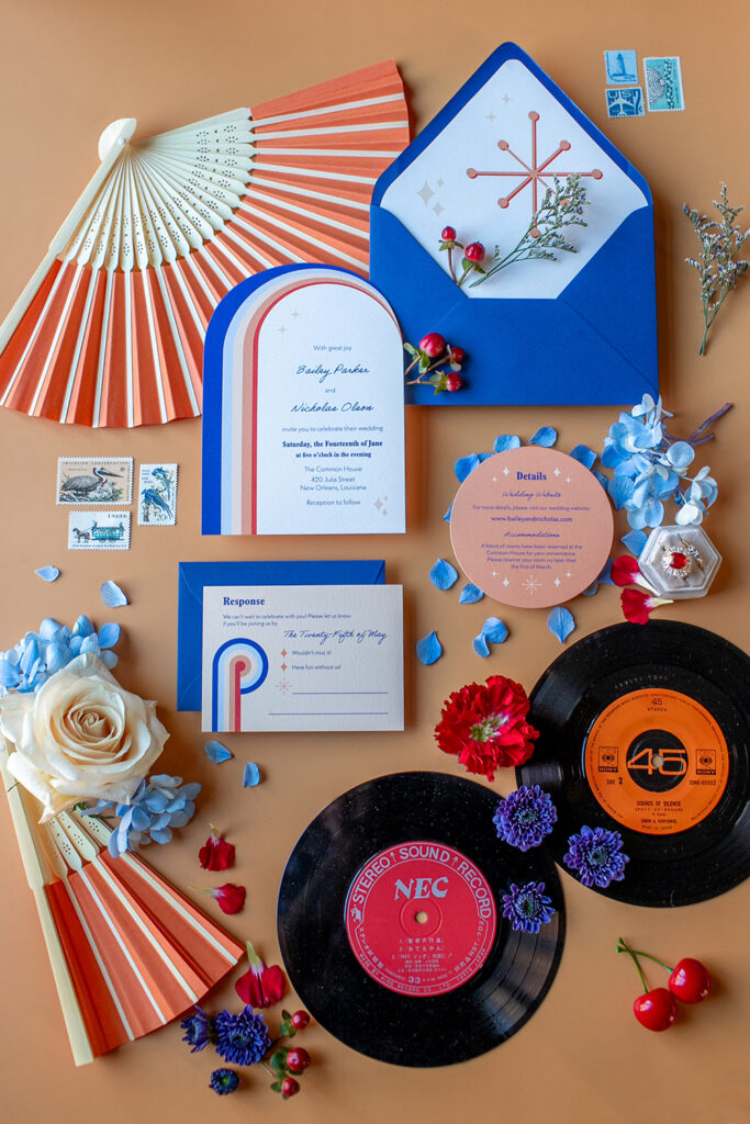 Wedding invitations, fan, vintage records, envelopes, stamps, flowers, and cherries arranged on a tan background.