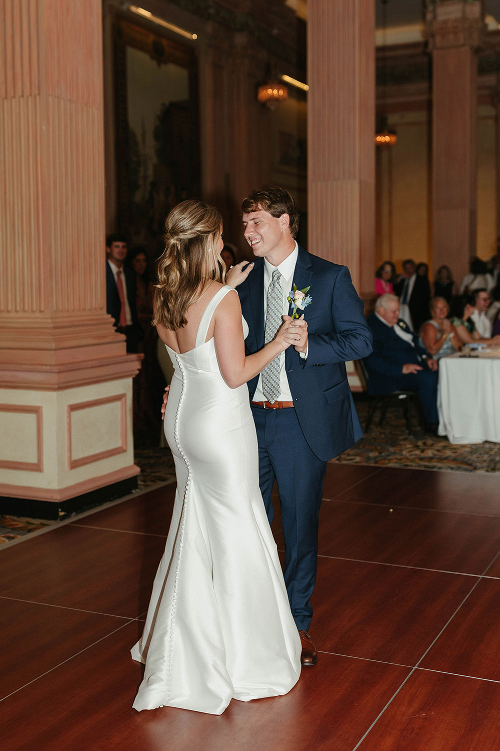 Bride and groom share their first dance together on the dance floor inside an elegant reception space.