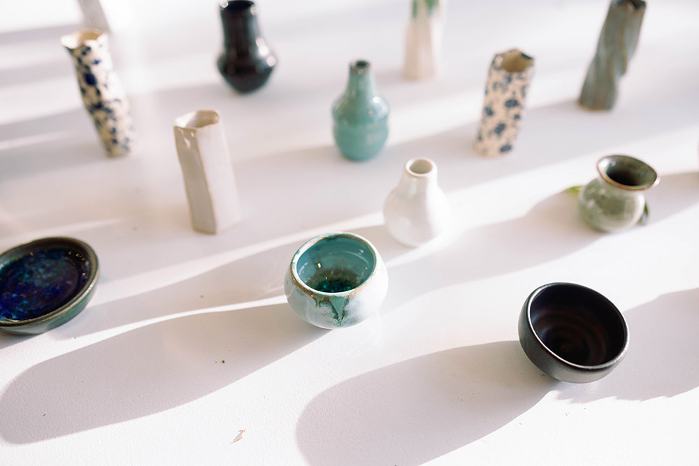 Close-up of assorted handmade ceramic mini vases and bowls displayed on a white surface in soft, natural light at a wedding reception.
