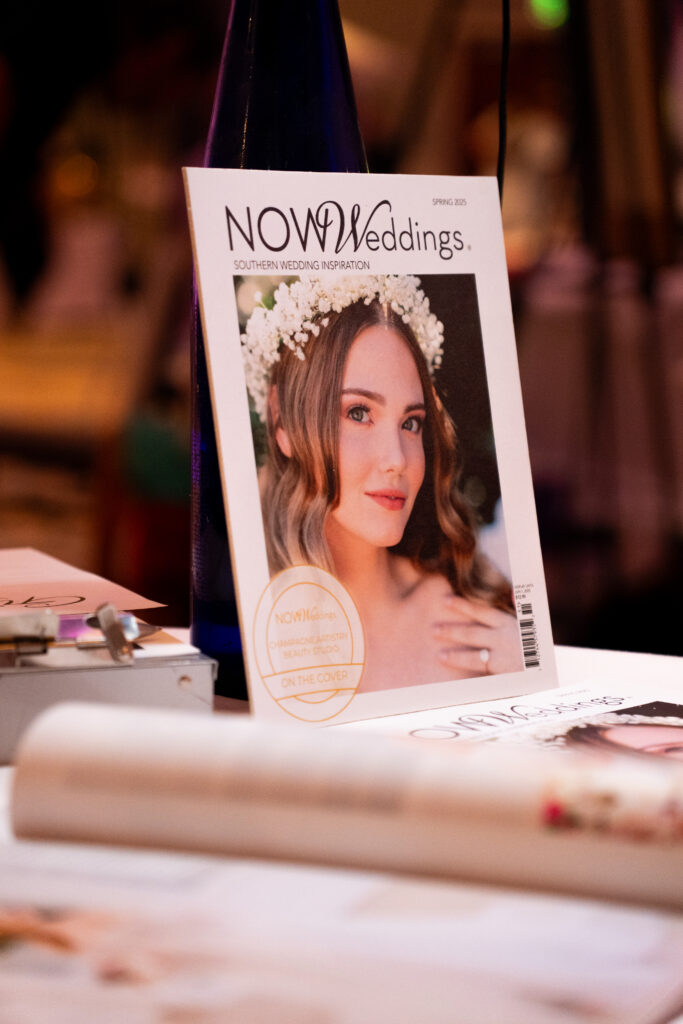 NOW Weddings magazine displayed on a tabletop at a bridal event, featuring a spring issue cover with a bride wearing a floral crown and soft bridal makeup.