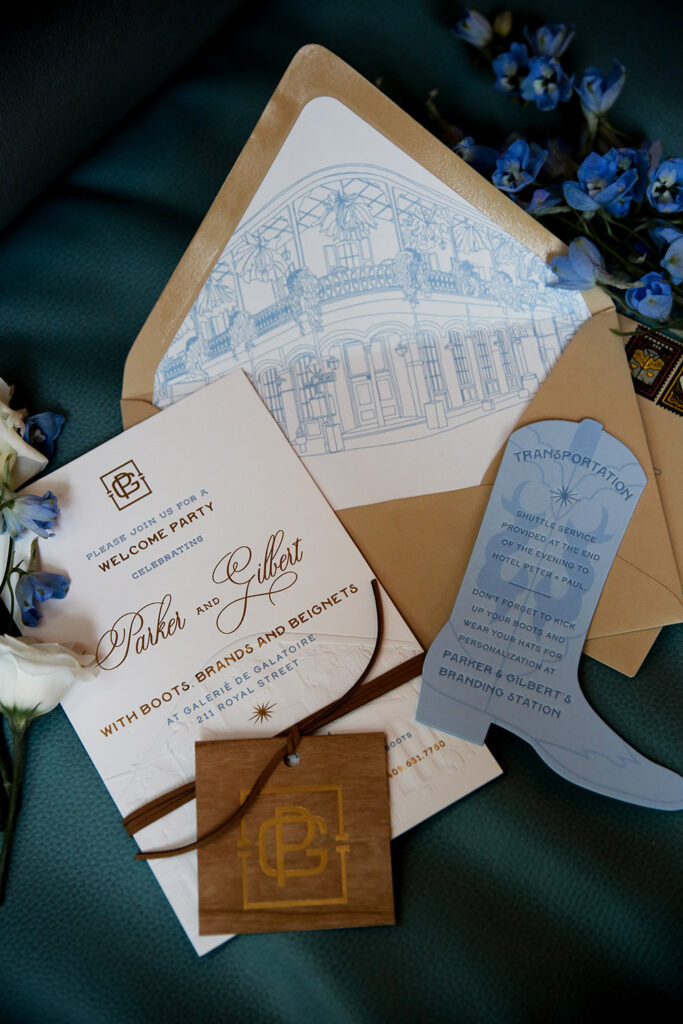 Flat lay of rehearsal dinner stationery featuring a welcome party invitation, envelope liner illustration, and blue transportation card with floral accents.