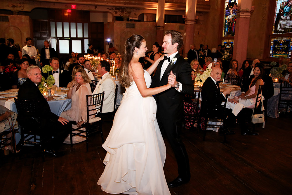 Bride and groom share their first dance during the reception, surrounded by seated guests and warm candlelight.