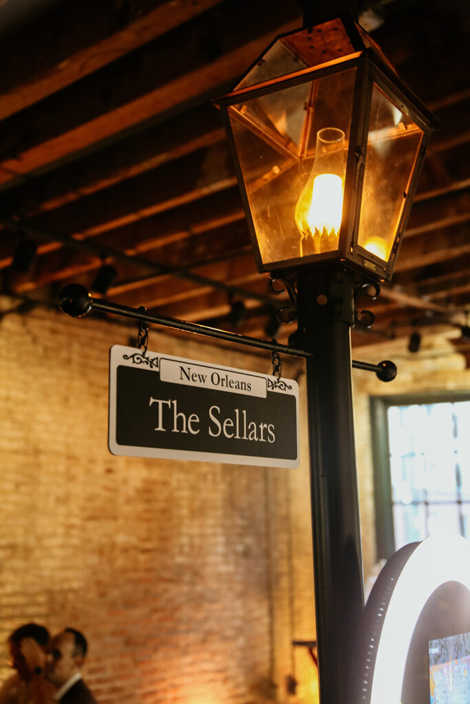 a vintage streetlamp with a hanging sign reading “New Orleans – The Sellars,” captured under exposed wooden beams at a New Orleans wedding venue.