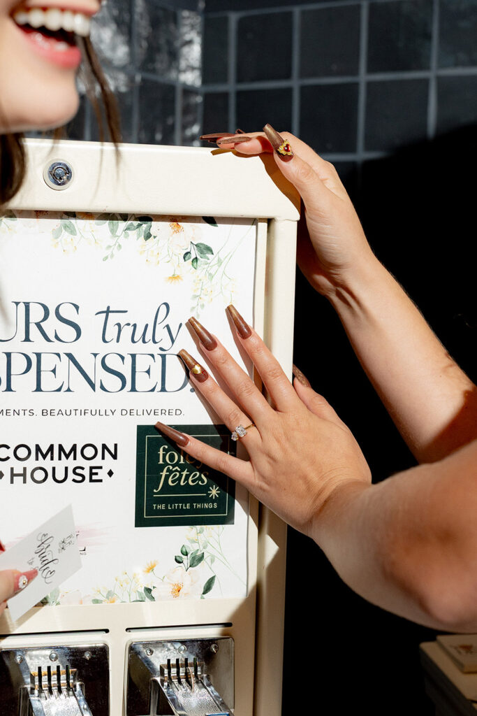 Close-up of a bride’s hand with an engagement ring pulling a vow from a vintage-style vow dispenser at a wedding reception.