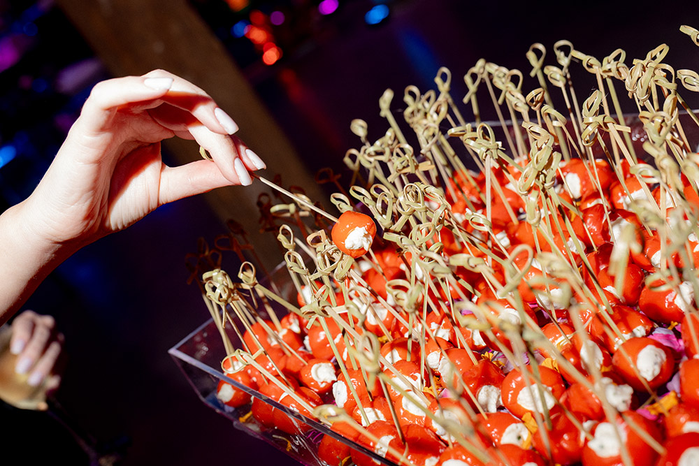 Hand reaching for a bite-size tomato and cheese skewer from a colorful display of cocktail appetizers.