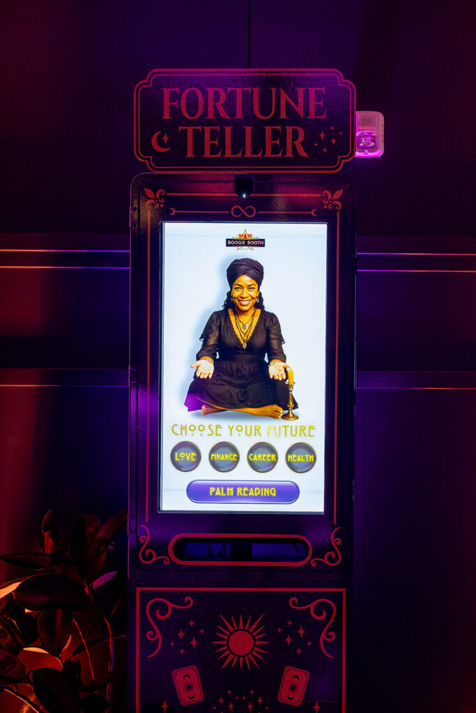 Interactive fortune teller photo booth with glowing screen and palm reading options at a wedding reception.