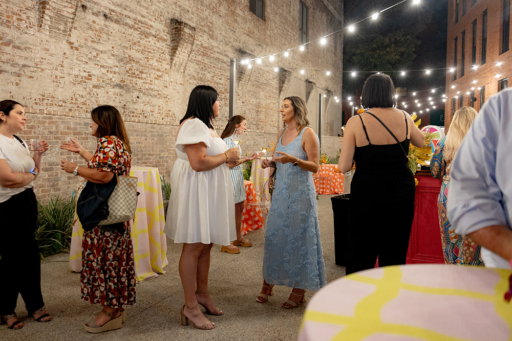 Wedding guests mingle and chat in an outdoor courtyard at night under string lights during a reception.
