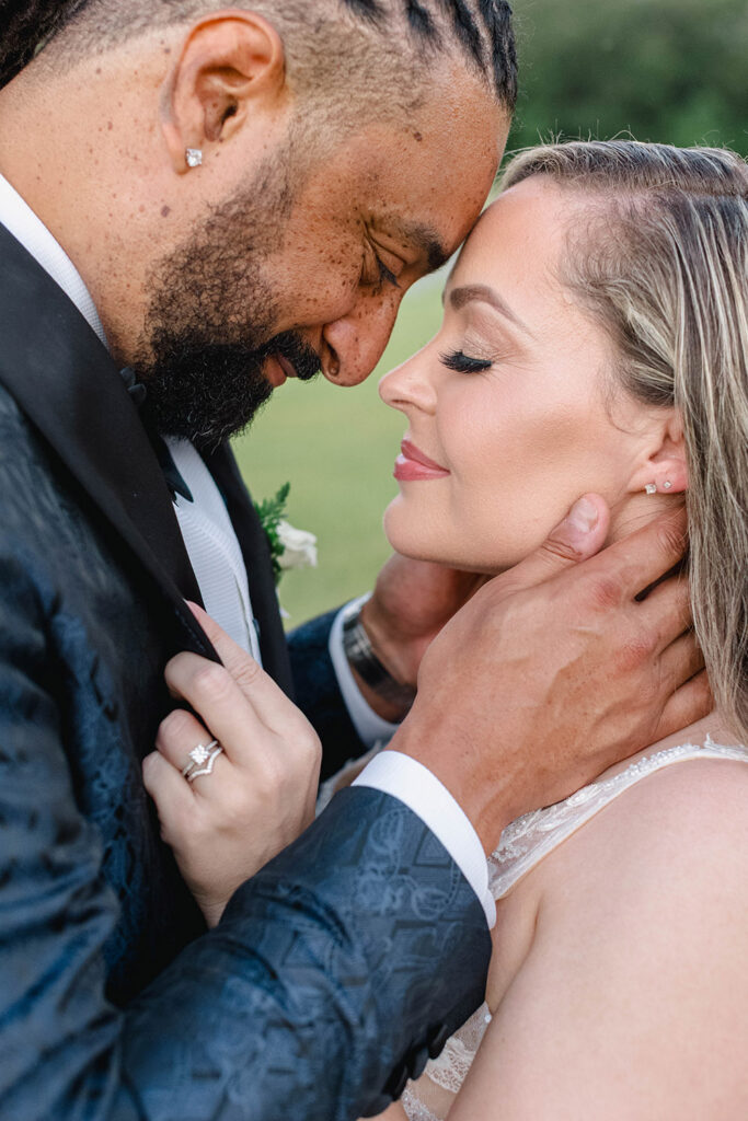 Close-up of the bride and groom touching foreheads, with the groom gently holding the bride’s face during an intimate moment outdoors.