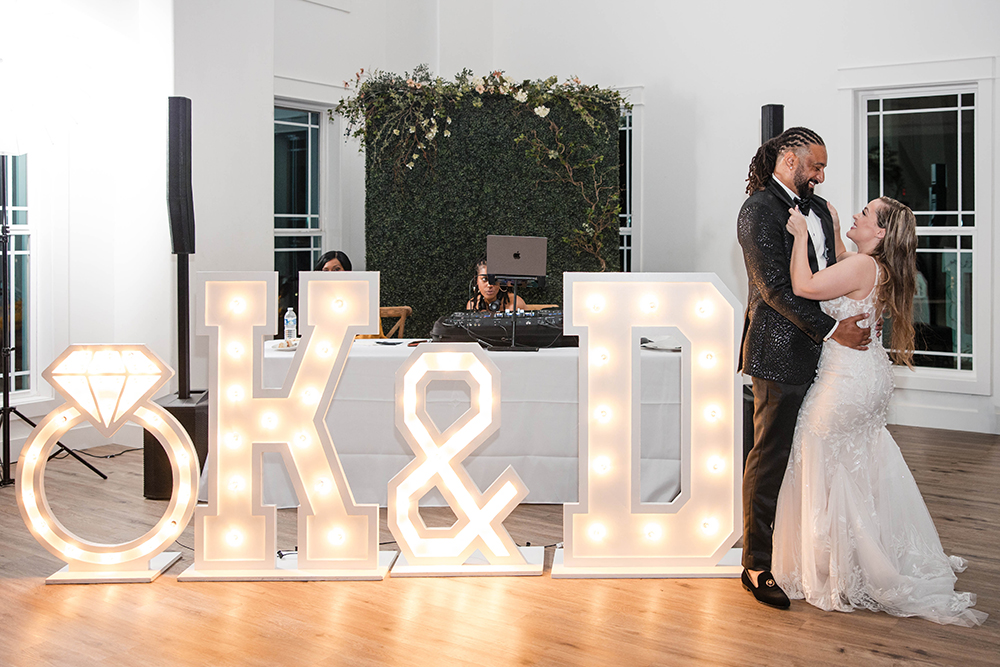 Illuminated marquee letters spelling “K & D” with a diamond ring icon, displayed indoors at a wedding reception.