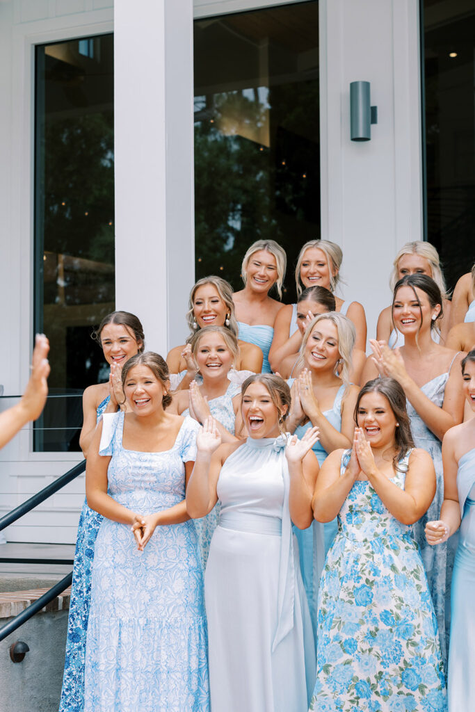 “Bridesmaids in light blue dresses cheer and smile with excitement during a first look moment at an outdoor wedding venue.”