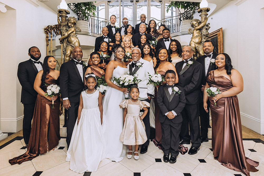 A large family portrait featuring the bride and groom surrounded by loved ones, with children and wedding party members gathered on a grand staircase.