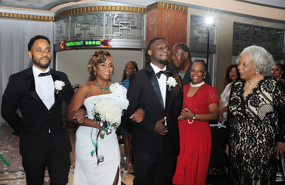 Bride walks down the aisle with family members during her wedding ceremony as guests look on.