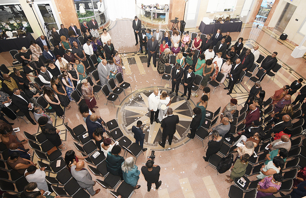 Overhead view of the wedding ceremony with the bride and groom standing at the center, surrounded by guests in a circular seating arrangement.