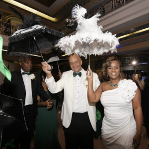 Bride and groom make a joyful entrance holding feathered umbrellas during their wedding celebration.