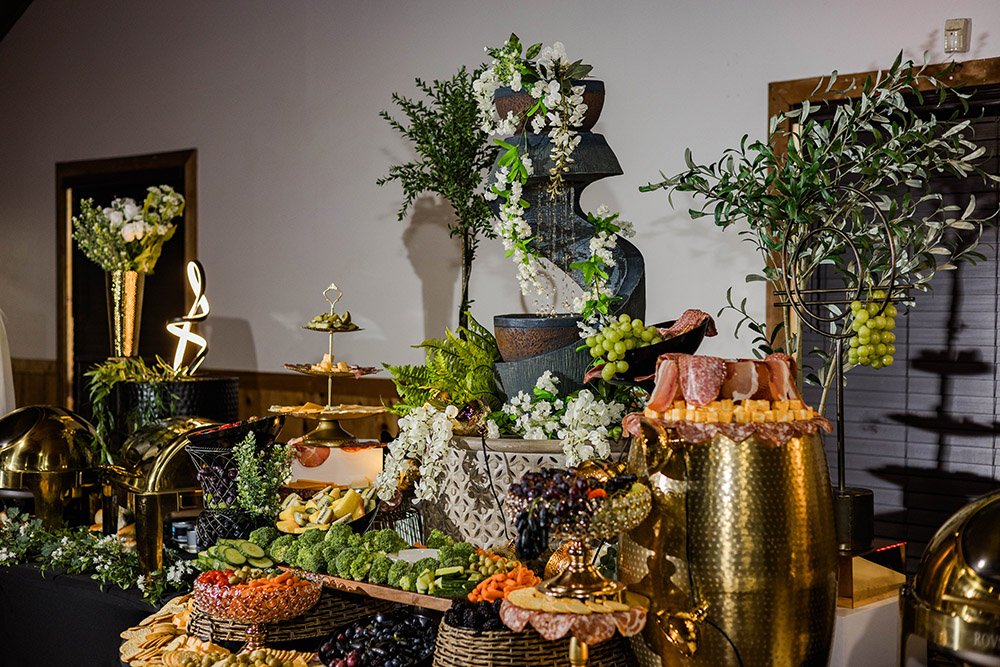 Lavish grazing table with charcuterie, fruit, greenery, and decorative displays.
