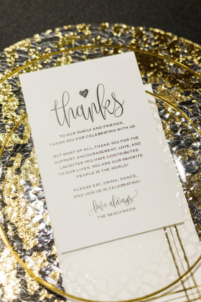 Elegant thank-you card displayed on a gold charger with textured black linens.