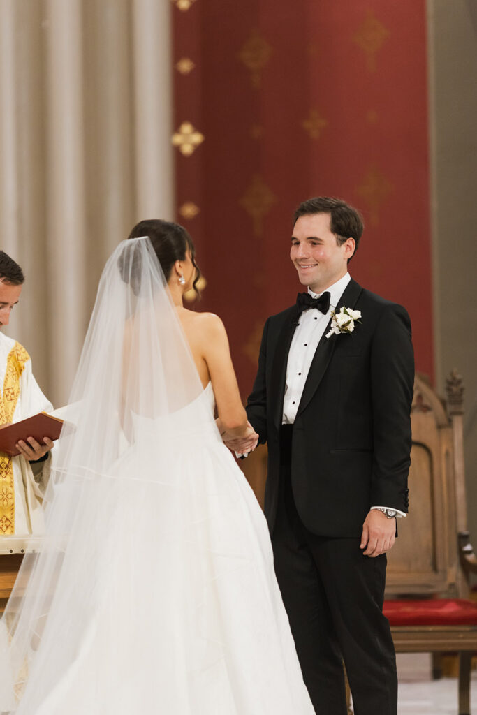 The bride and groom face one another at the altar during their ceremony, holding hands as the officiant stands beside them.