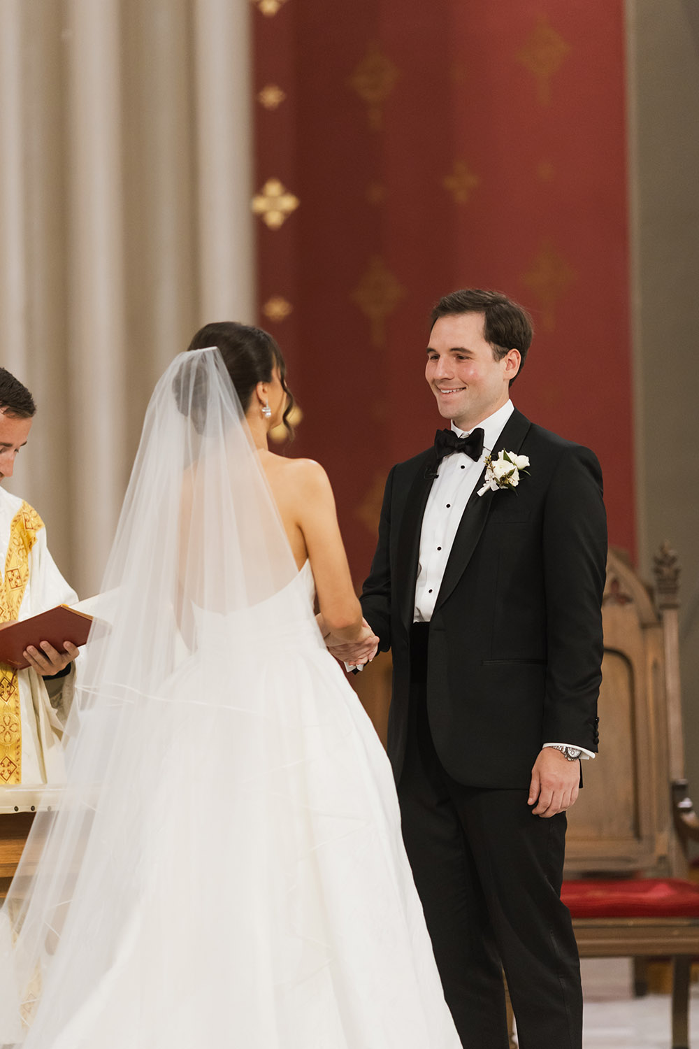 The bride and groom face one another at the altar during their ceremony, holding hands as the officiant stands beside them.