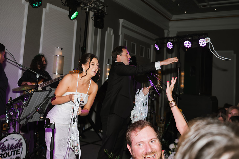 The newlyweds toss beads from the stage during the reception as a live band plays and guests reach up cheering.