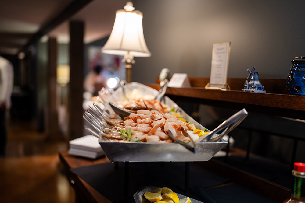 A chilled shrimp cocktail display with lemon wedges and serving tongs set on a reception buffet table.