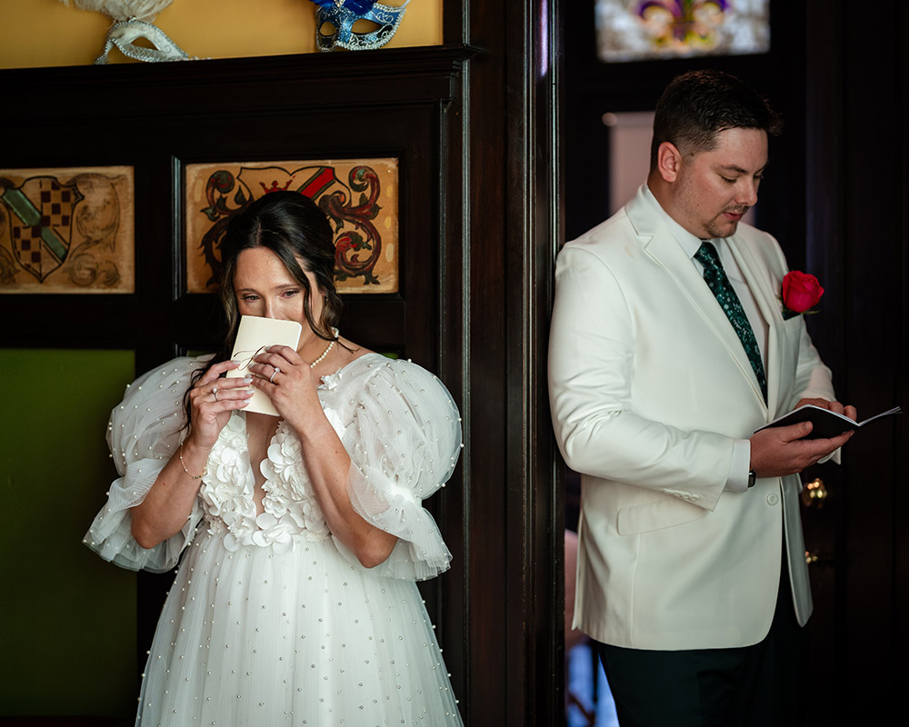 First look letters moment with the bride and groom standing back-to-back indoors, each reading handwritten notes before the ceremony.