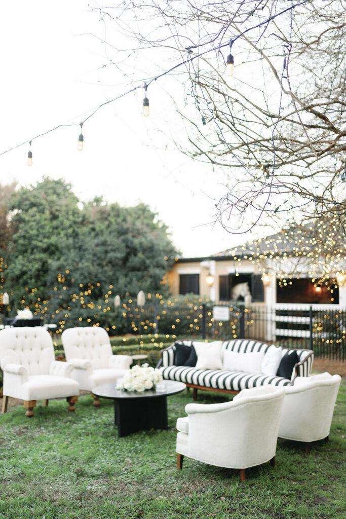 Outdoor wedding lounge seating with white sofas, bistro lights, and greenery set for the reception.