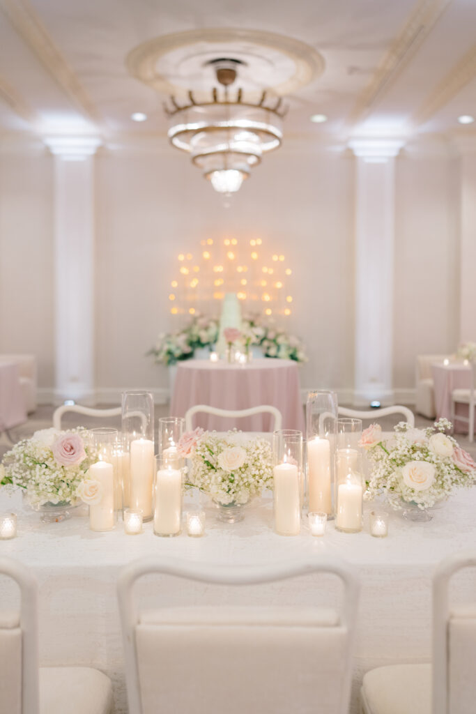 Elegant head table styled with blush linens, low floral arrangements, and glowing pillar candles beneath a crystal chandelier.