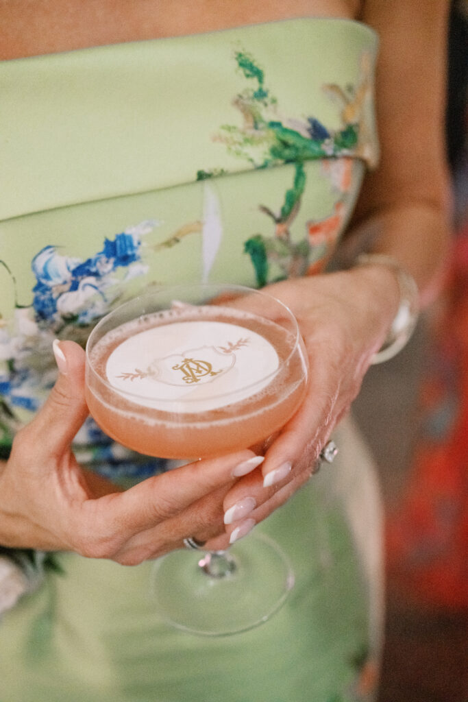 Close-up of a signature cocktail topped with a custom monogram foam garnish, held in a coupe glass.