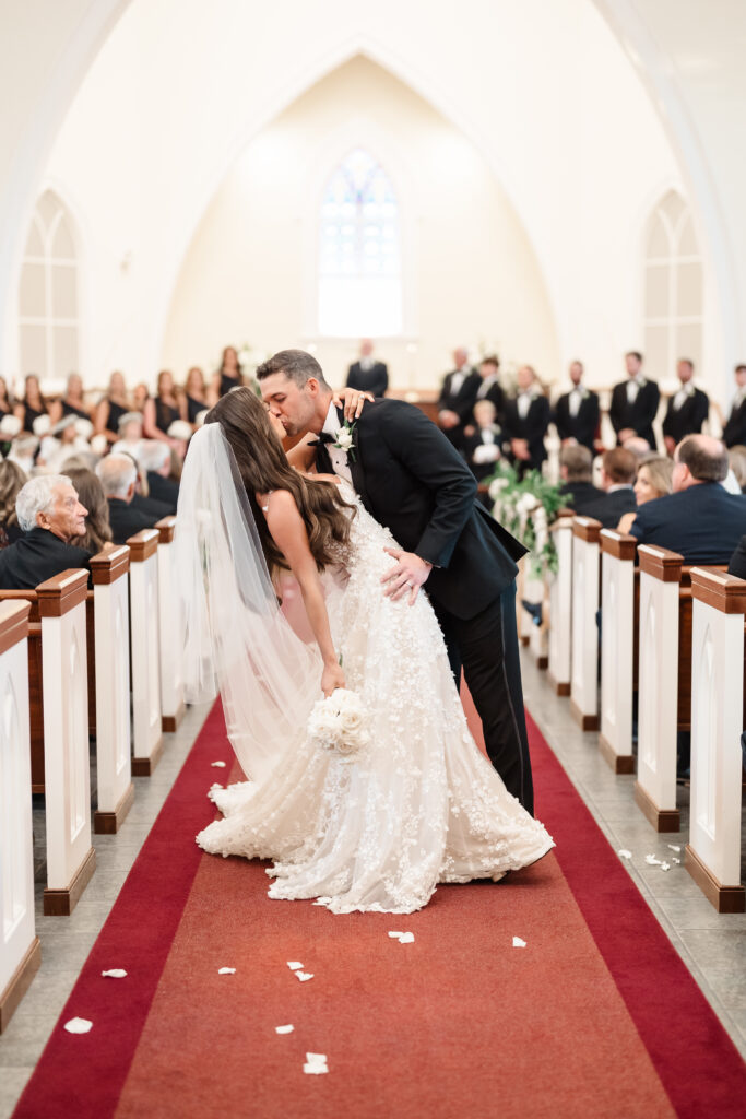 Bride and groom sharing their first kiss in the church aisle as guests look on during the ceremony.