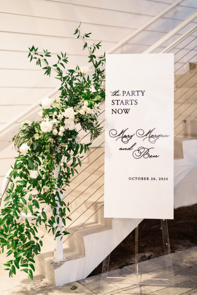 Modern welcome sign framed by cascading greenery announcing the couple’s wedding celebration and date.