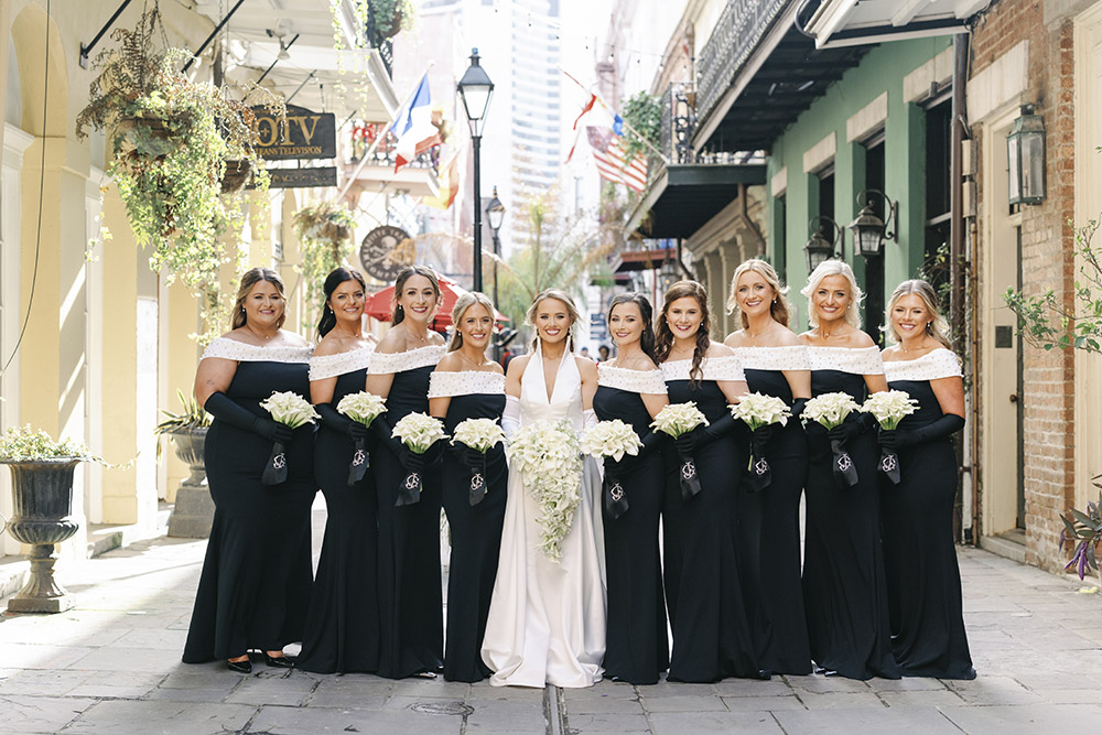 Bride poses with her bridesmaids in matching black off-the-shoulder gowns on a classic New Orleans street.