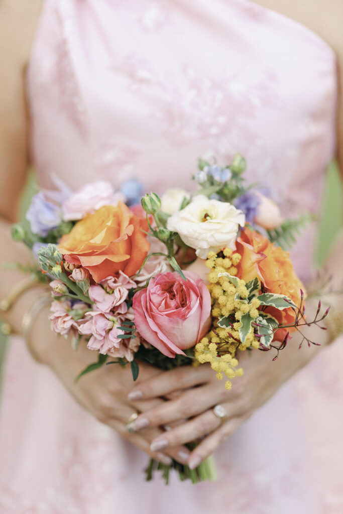 Bridesmaid holding a vibrant bouquet of coral, blush, and yellow flowers in a soft pink dress.