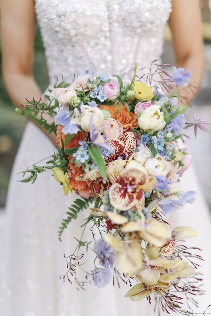 Bride holding a cascading bouquet of pastel blooms with orchids and garden-style florals.