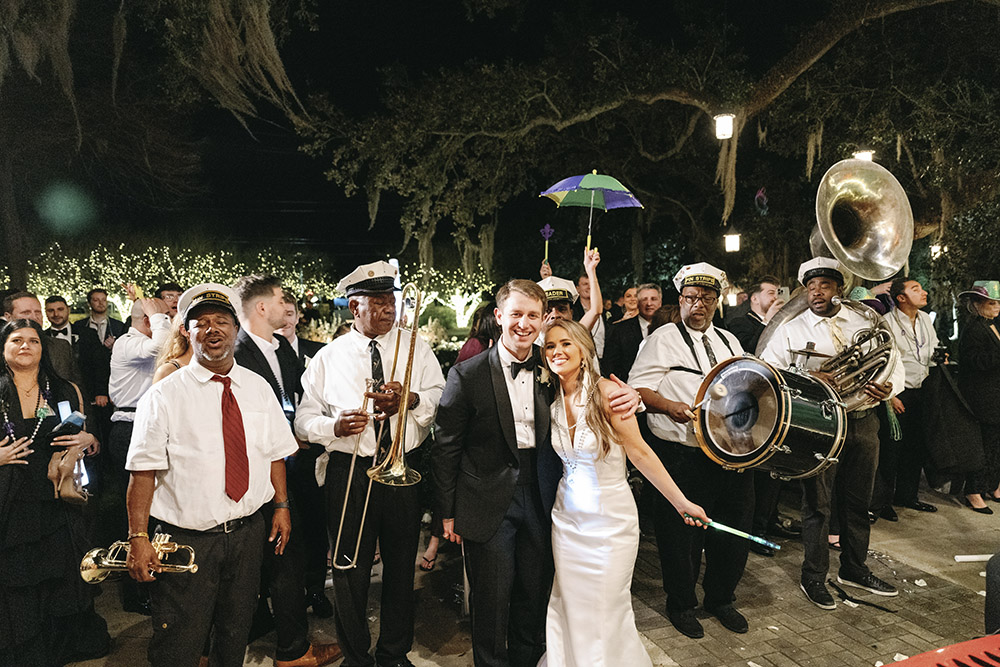 Bride and groom leading a second line parade with a brass band and cheering guests at a New Orleans wedding.