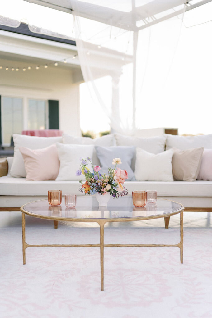 Reception lounge seating with white sofas, pastel accent pillows, and a glass coffee table topped with a floral arrangement.