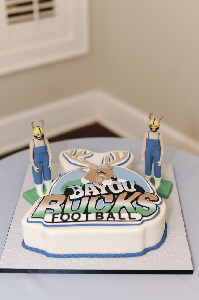 Custom groom’s cake inspired by Bayou Bucks football, topped with playful figurines and bold team detailing.