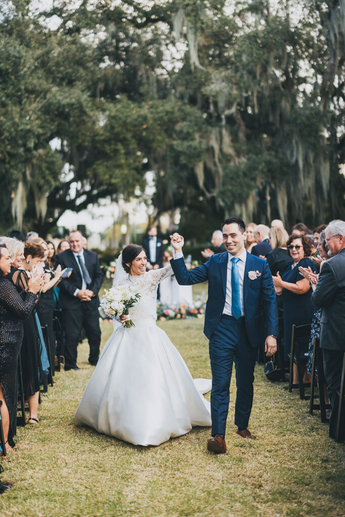 Bride and groom walking hand in hand down the aisle following the ceremony as guests applaud on either side.