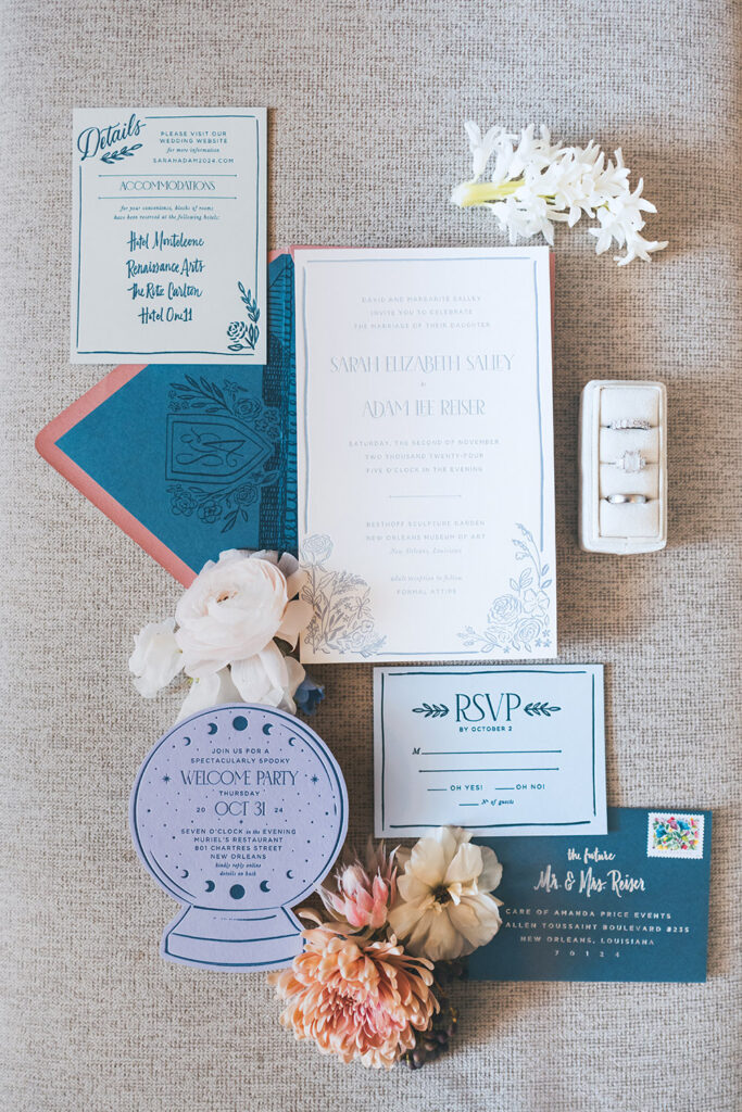 Wedding invitation suite with blue and ivory stationery, RSVP card, envelope, and rings styled with soft florals.