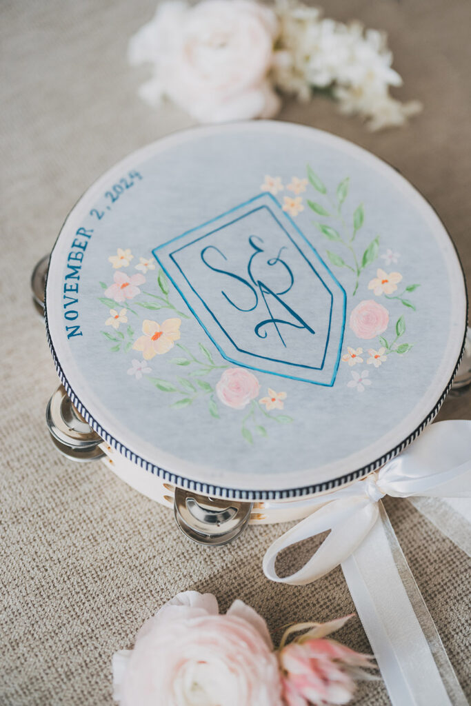 Hand-painted wedding tambourine featuring the couple’s monogram and wedding date, styled with blush blooms.