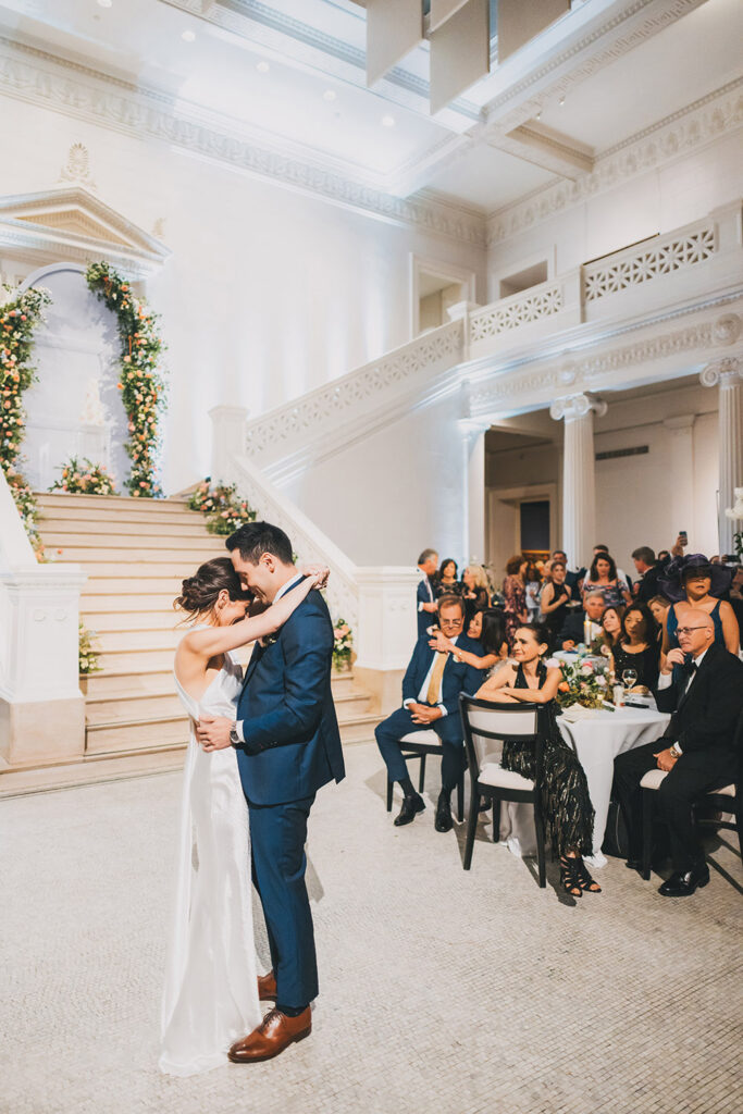 Bride and groom sharing their first dance on the museum floor as guests look on from candlelit tables beneath soaring ceilings.