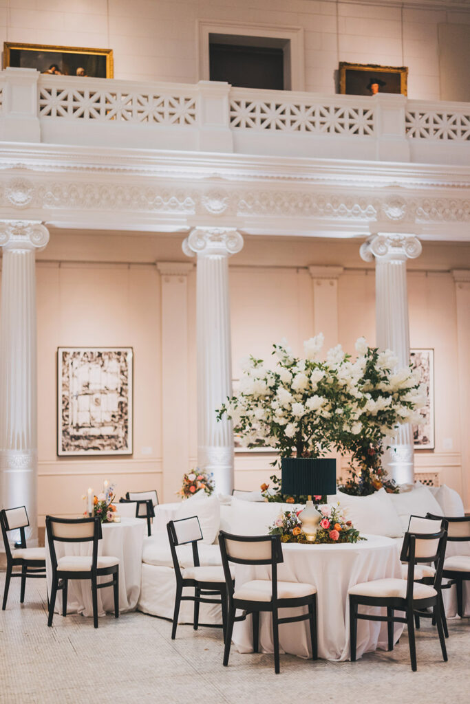 Museum reception tables styled with white linens, black chairs, candlelight, and low floral centerpieces.