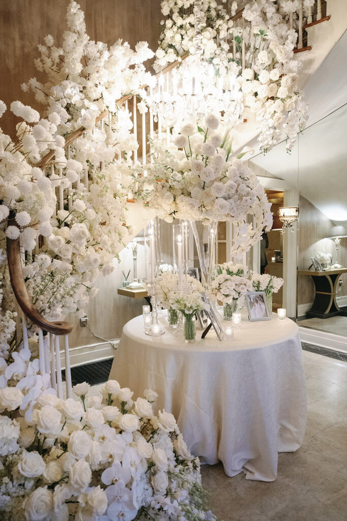 Floral staircase display with cascading white roses, orchids, and candles surrounding a welcome table at a luxury wedding reception.