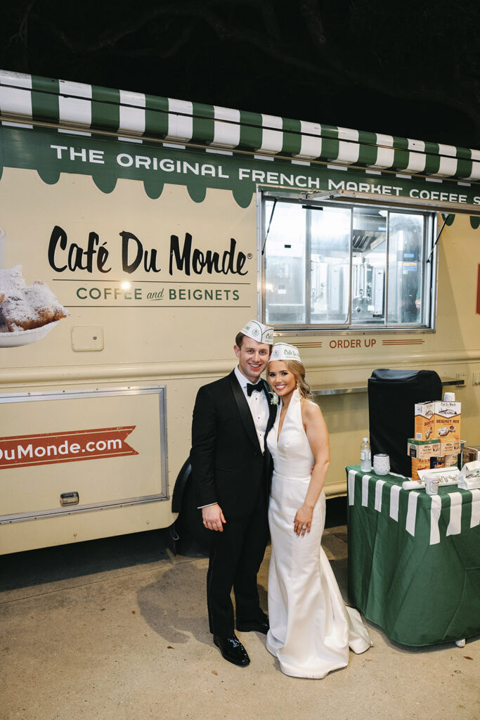 Bride and groom posing in front of a Café du Monde beignet truck during a New Orleans wedding celebration.
