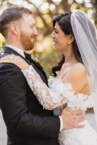Romantic close-up portrait of the bride and groom smiling at each other beneath soft golden light.