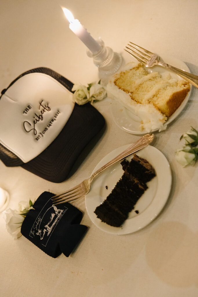 Wedding reception table with slices of vanilla and chocolate cake, candlelight, and custom “The Saiberts” wedding hat favor.